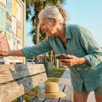 A senior woman in Florida looks at a community bulletin board for local job opportunities in the warm afternoon sun.