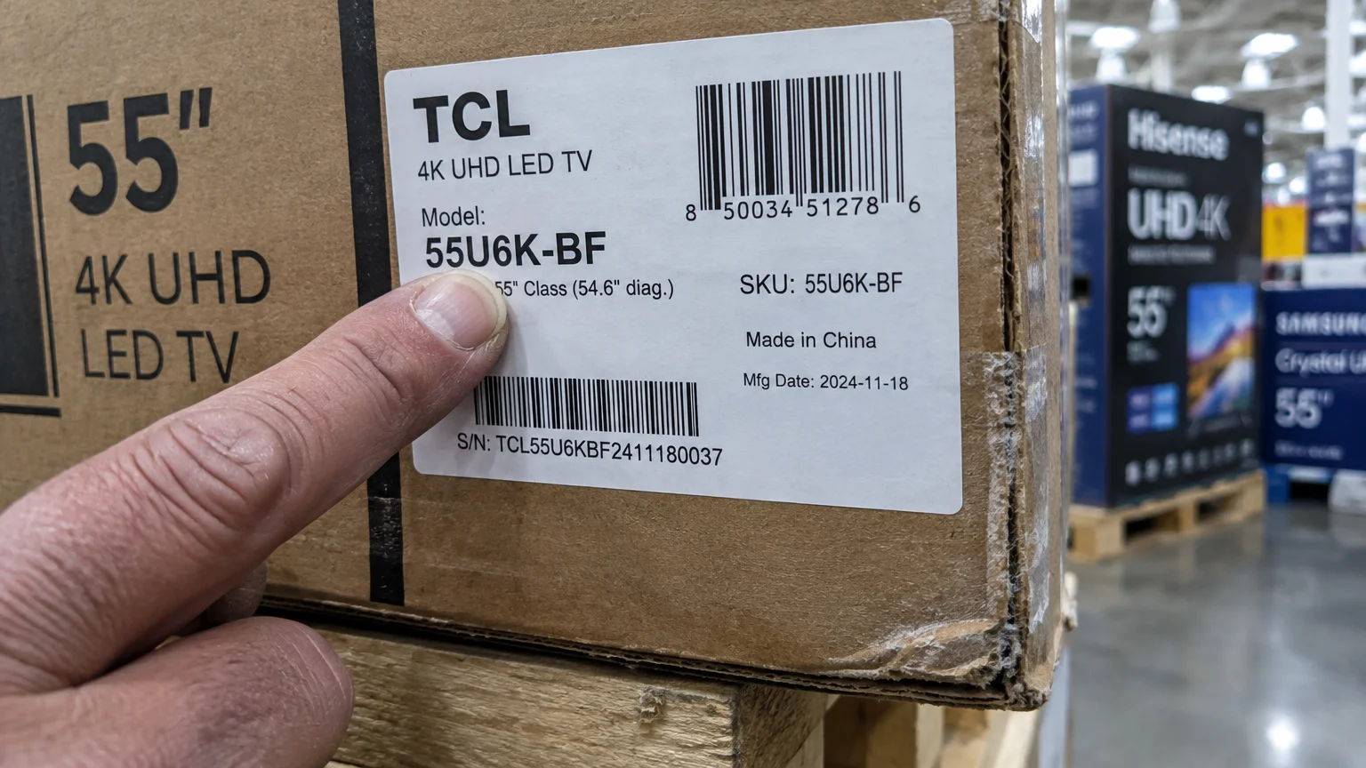 A person points to a label on a cardboard television box showing the model number 55U6K-BF in a store aisle.