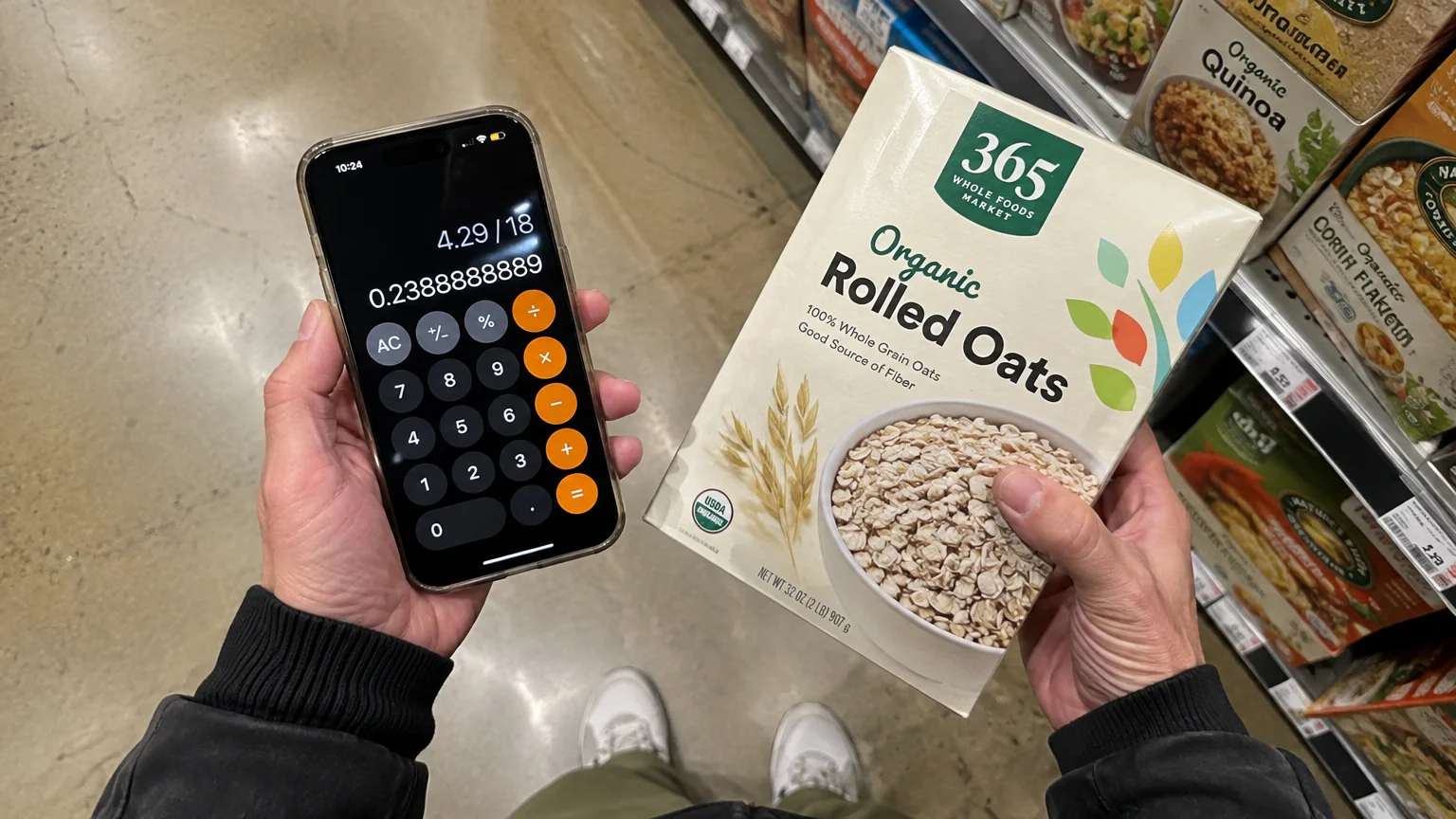 Hands holding a smartphone calculator displaying division alongside a box of Whole Foods rolled oats in a store aisle.